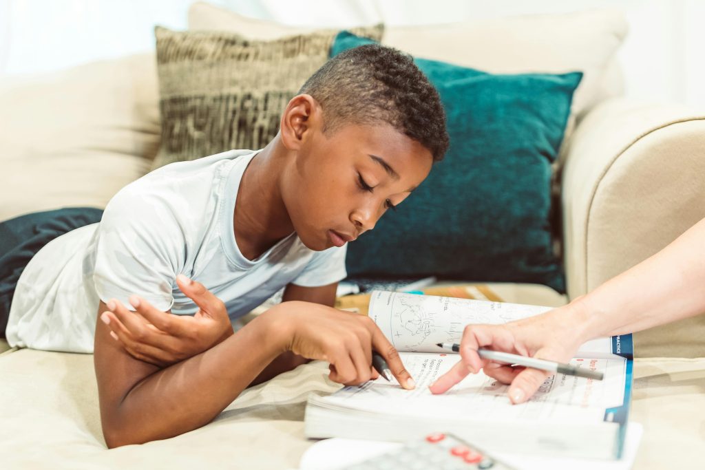 A young boy intently studying a book with guidance on a comfortable couch indoors.