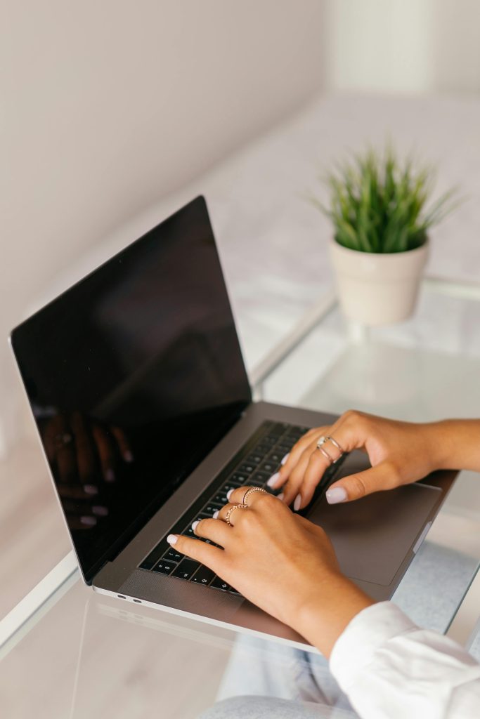 Close-up of woman's hands typing on a laptop at a glass table. Modern and minimalistic setting.